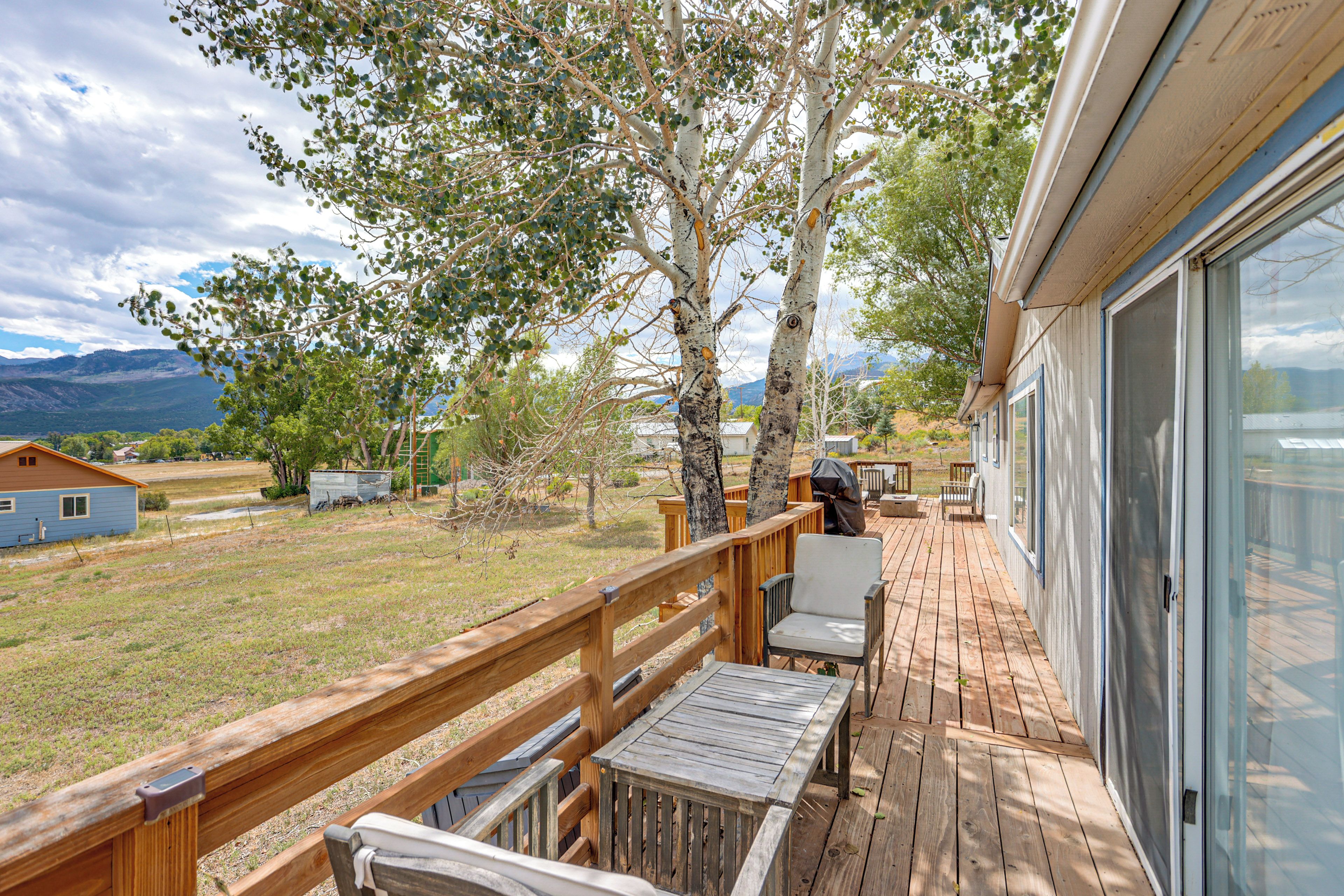 A wooden deck with outdoor furniture, overlooking a grassy area with trees and a distant mountain range.