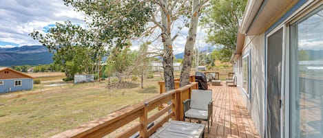 A wooden deck with outdoor furniture, overlooking a grassy area with trees and a distant mountain range.