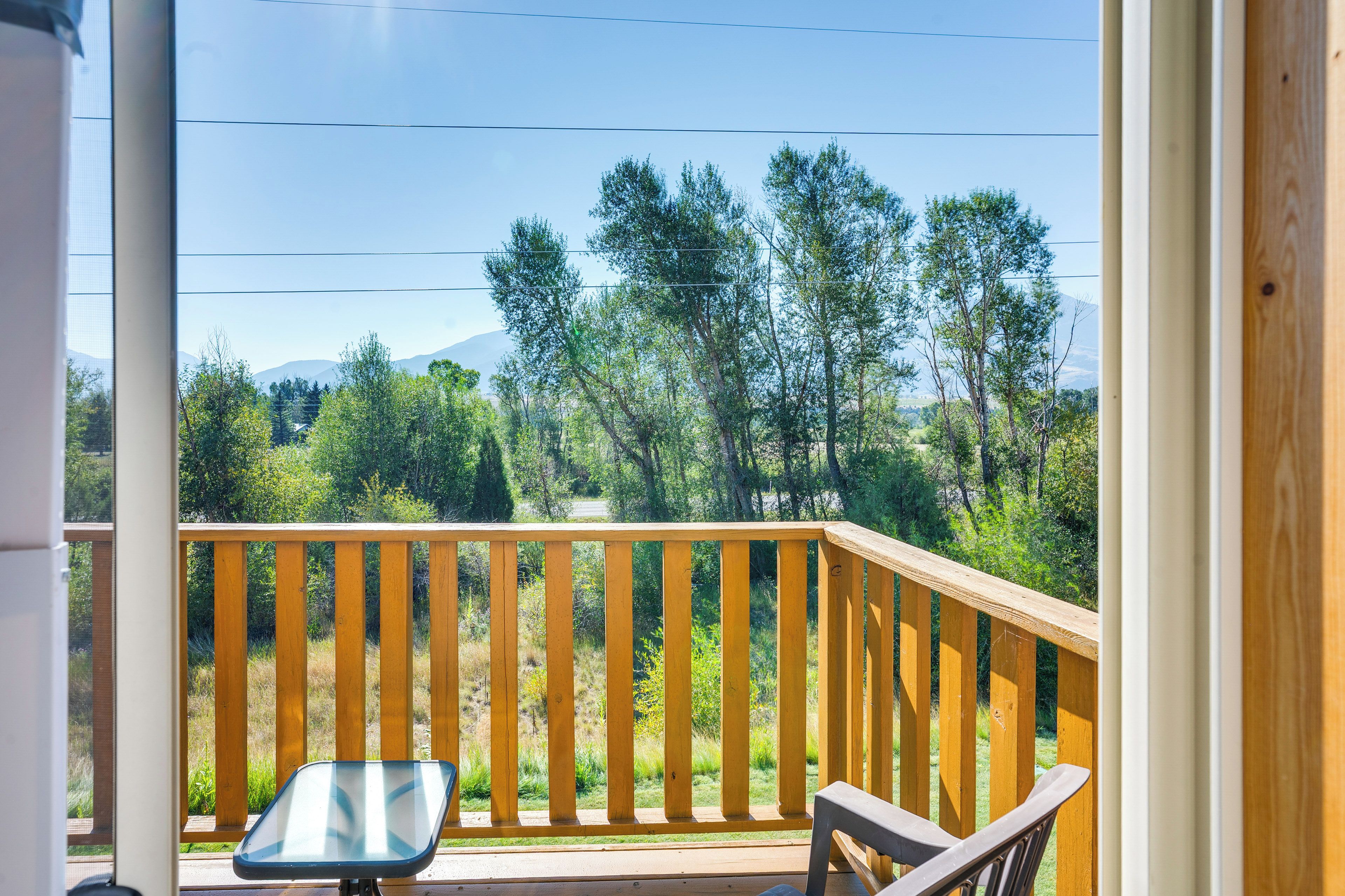 A balcony with a table and chair, overlooking a forested area with mountains in the distance.