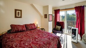 Quarto com uma cama grande, uma cadeira, uma mesa, um abajur e uma janela com cortinas.
