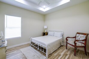 A bedroom with a bed, a chair, a nightstand, a lamp, and a window. - Single Home: Spacex, Hwy 511 & Beaches (Brownsville)