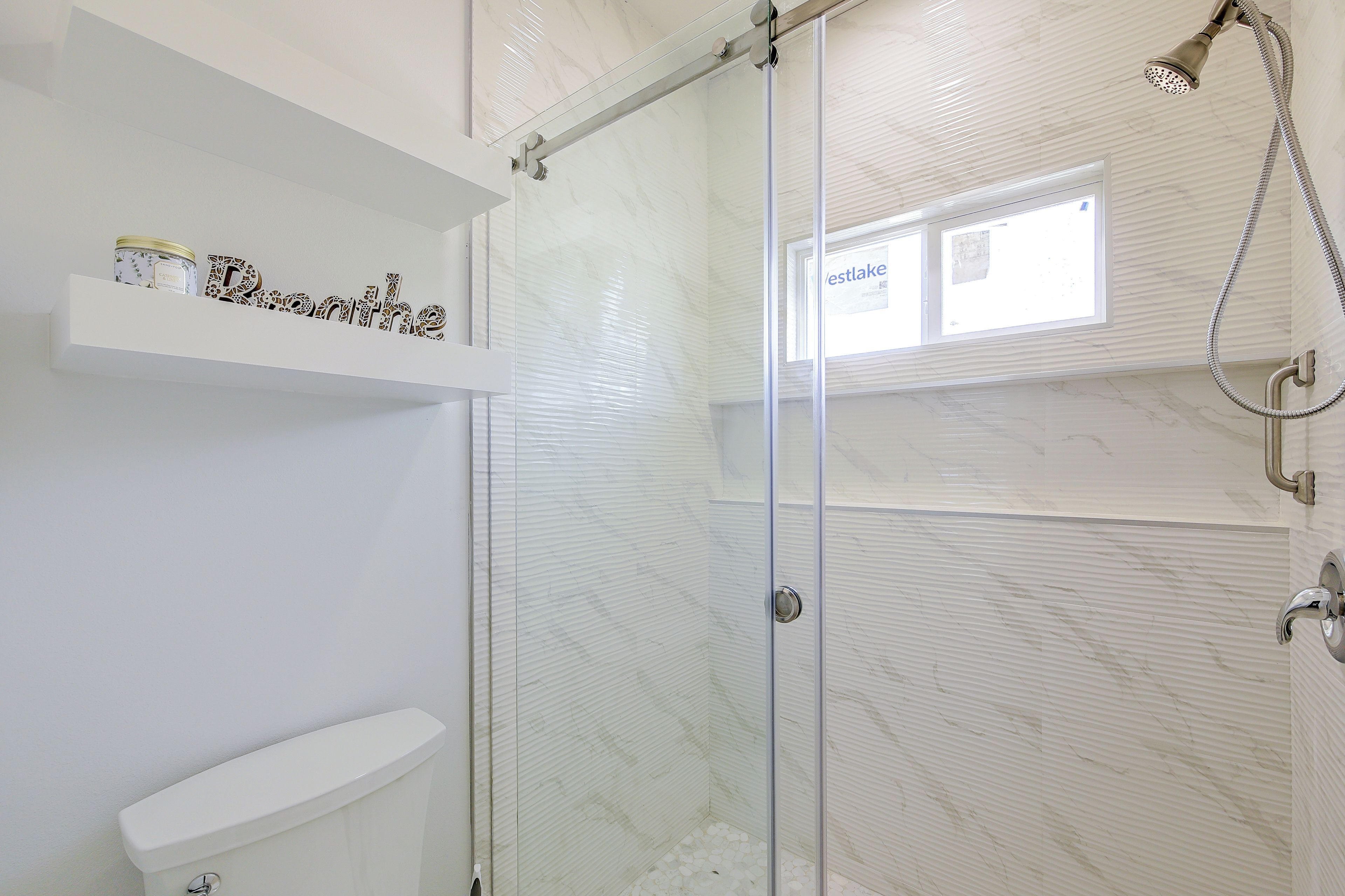 Een moderne badkamer met een douchecabine van glas, een toilet en een plank met toiletartikelen.
