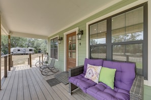 A covered porch with a purple sofa, rocking chairs, and a view of a trailer park. - Boutique Retreat Minutes From Round Top! (Fayetteville)