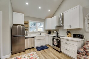 A modern kitchen with white cabinets, stainless steel appliances, a window, and a plaid-patterned chair. - Boutique Retreat Minutes From Round Top! (Fayetteville)