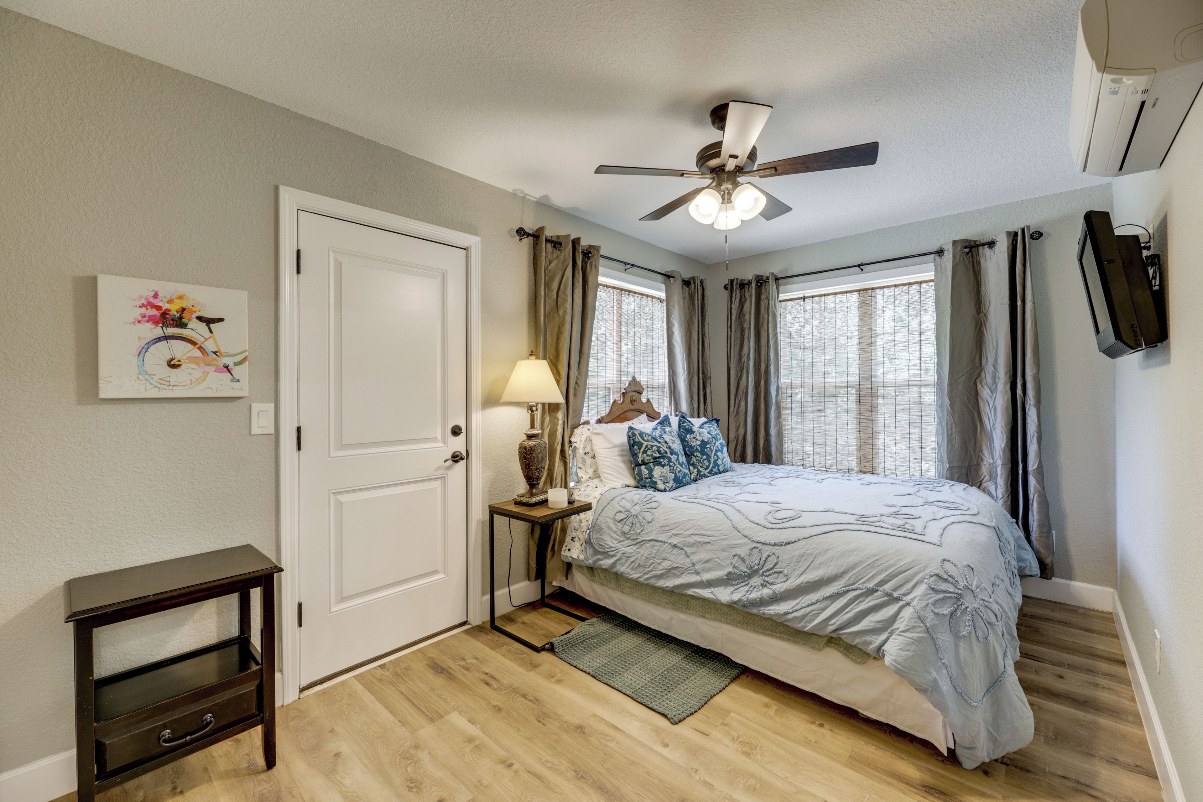 A bedroom with a bed, a nightstand, a lamp, a ceiling fan, and a painting on the wall.