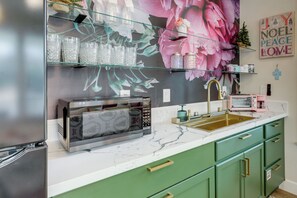 Una cocina con microondas, un lavabo y un estante de vidrio con objetos decorativos.