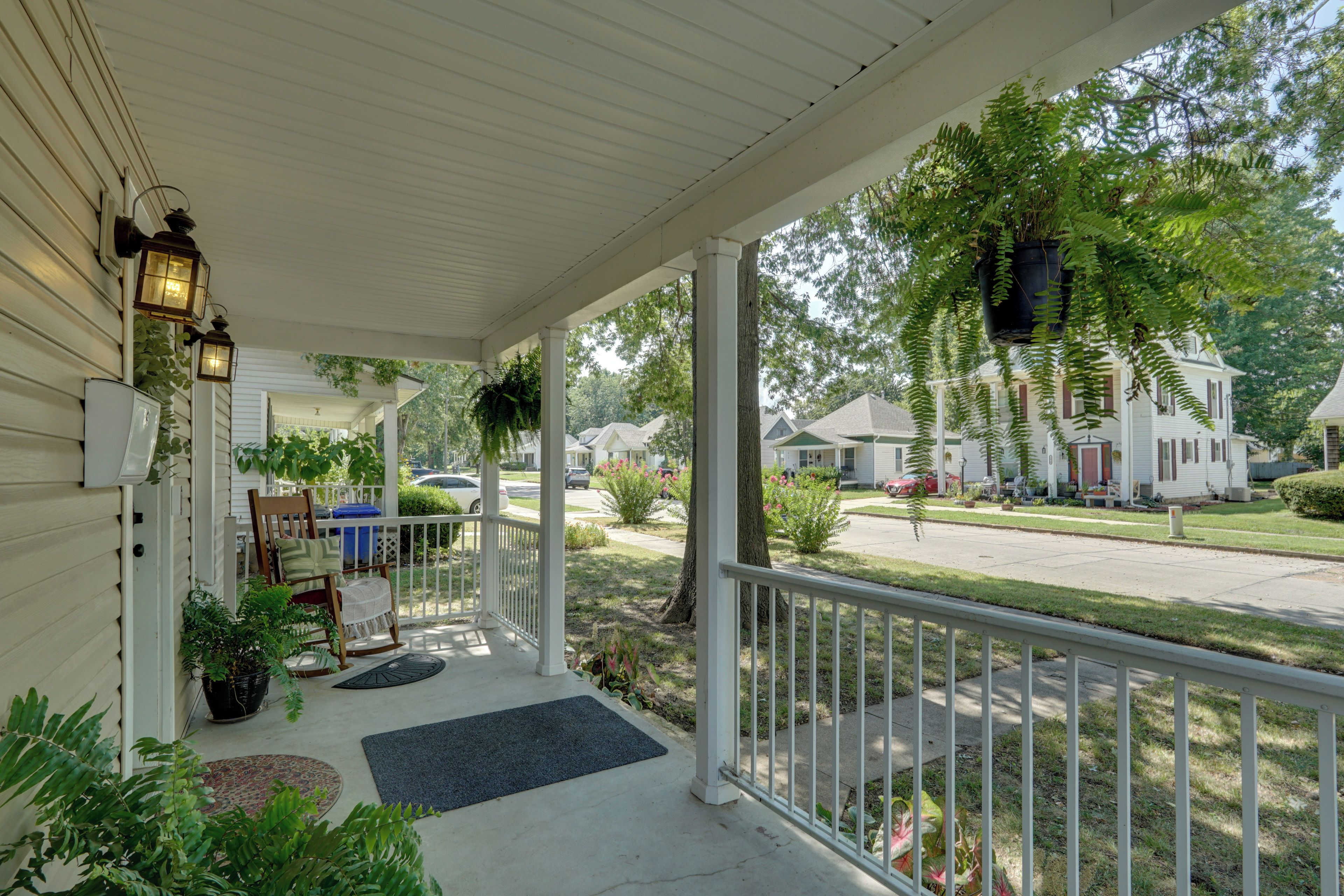 A covered porch with a white railing, potted plants, and a bench.