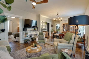 A spacious living room with a flat-screen TV, a dining area, and a kitchen in the background.