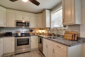 A kitchen with white cabinets, stainless steel appliances, granite countertops, and a window with blinds.