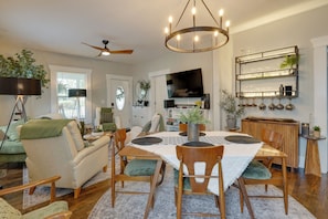 A modern living room with a dining area, a flat-screen TV, and a built-in shelf with glassware.