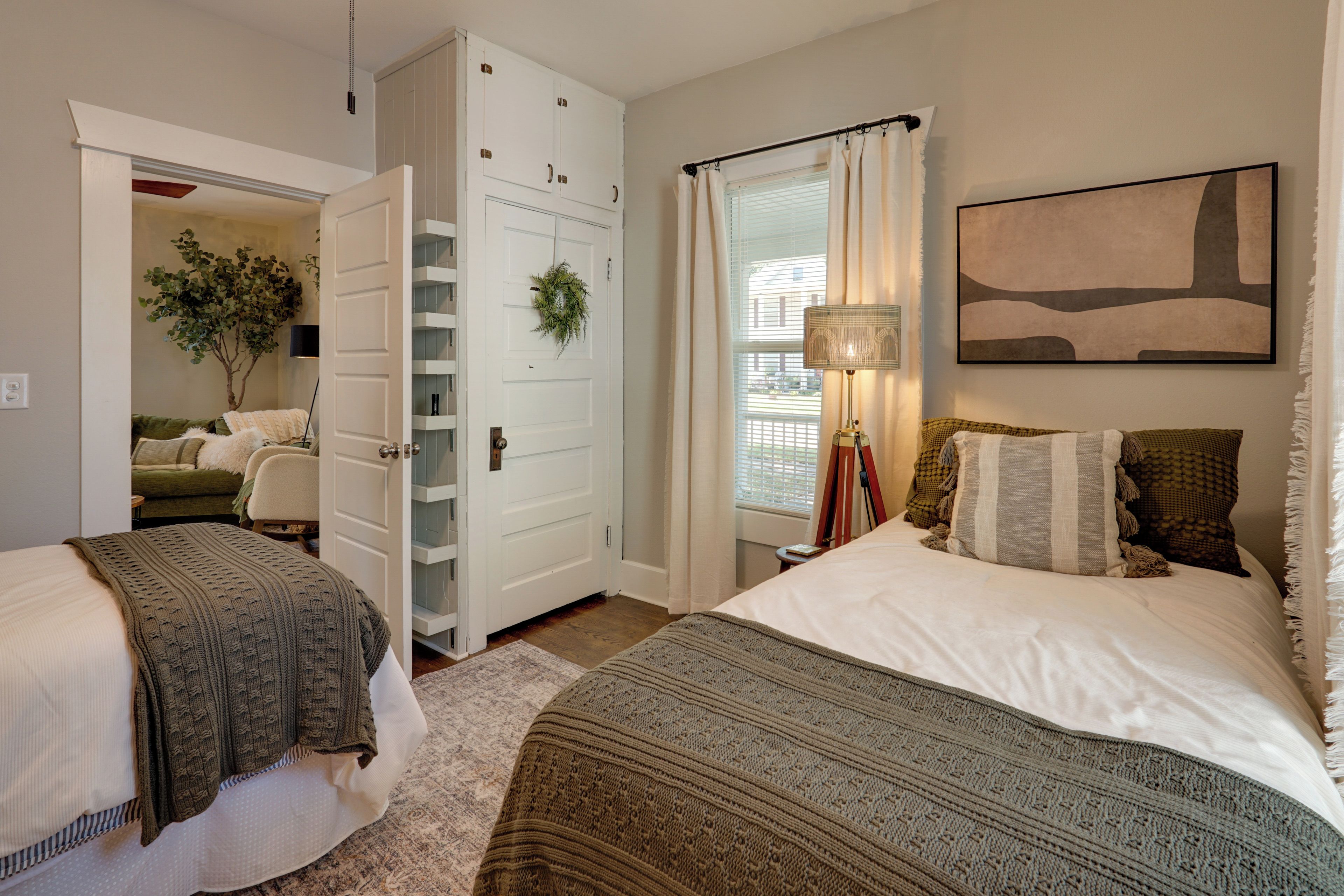 A bedroom with two beds, a wardrobe, a window with curtains, a lamp, and a painting on the wall.