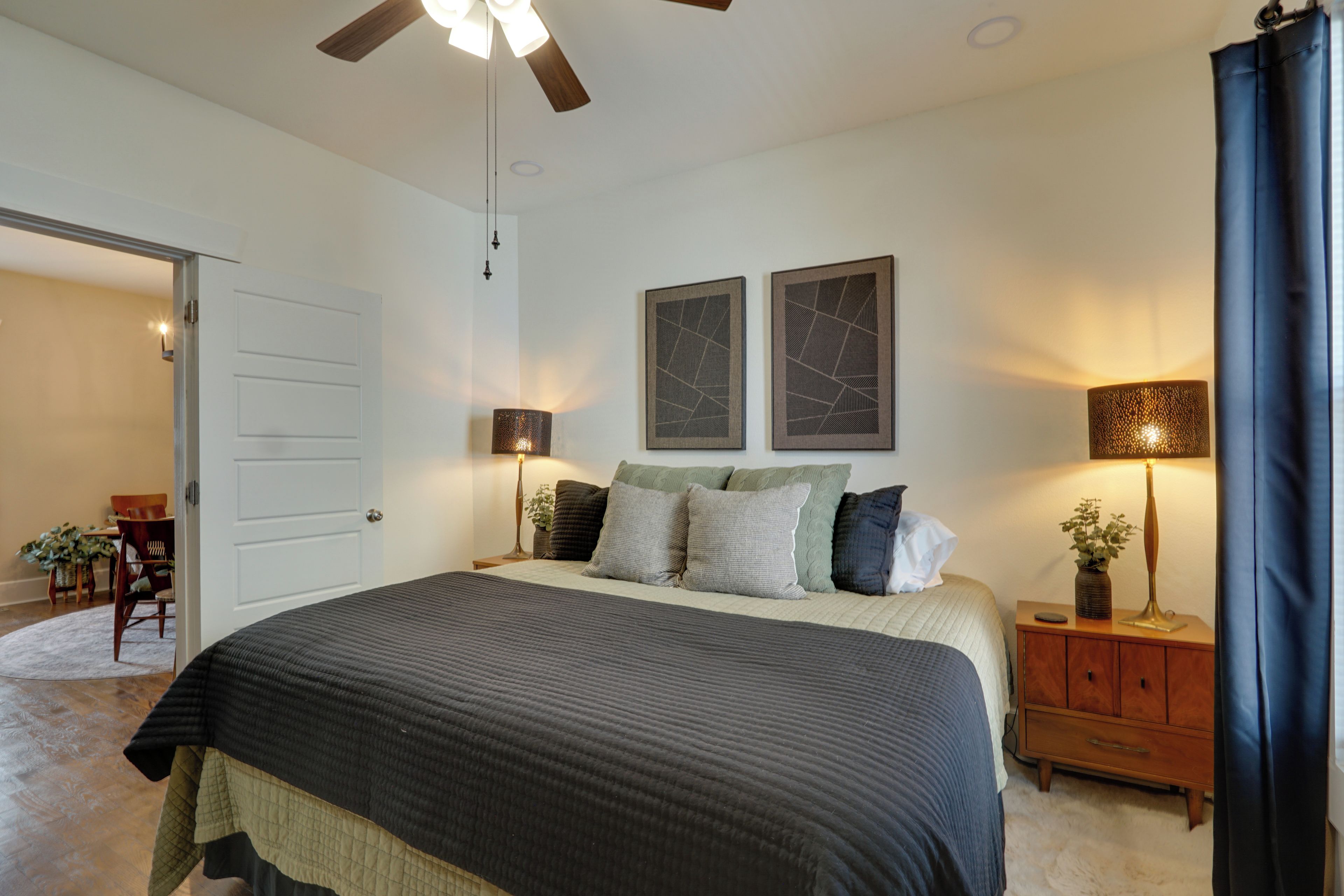 A bedroom with a bed, two wall-mounted lamps, a ceiling fan, and a door leading to another room.