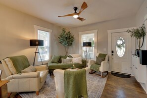 A living room with a green sofa, a white armchair, a floor lamp, and a ceiling fan.