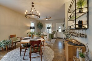 A spacious living room with a dining area, a ceiling fan, and a wall-mounted shelf with decorative items.