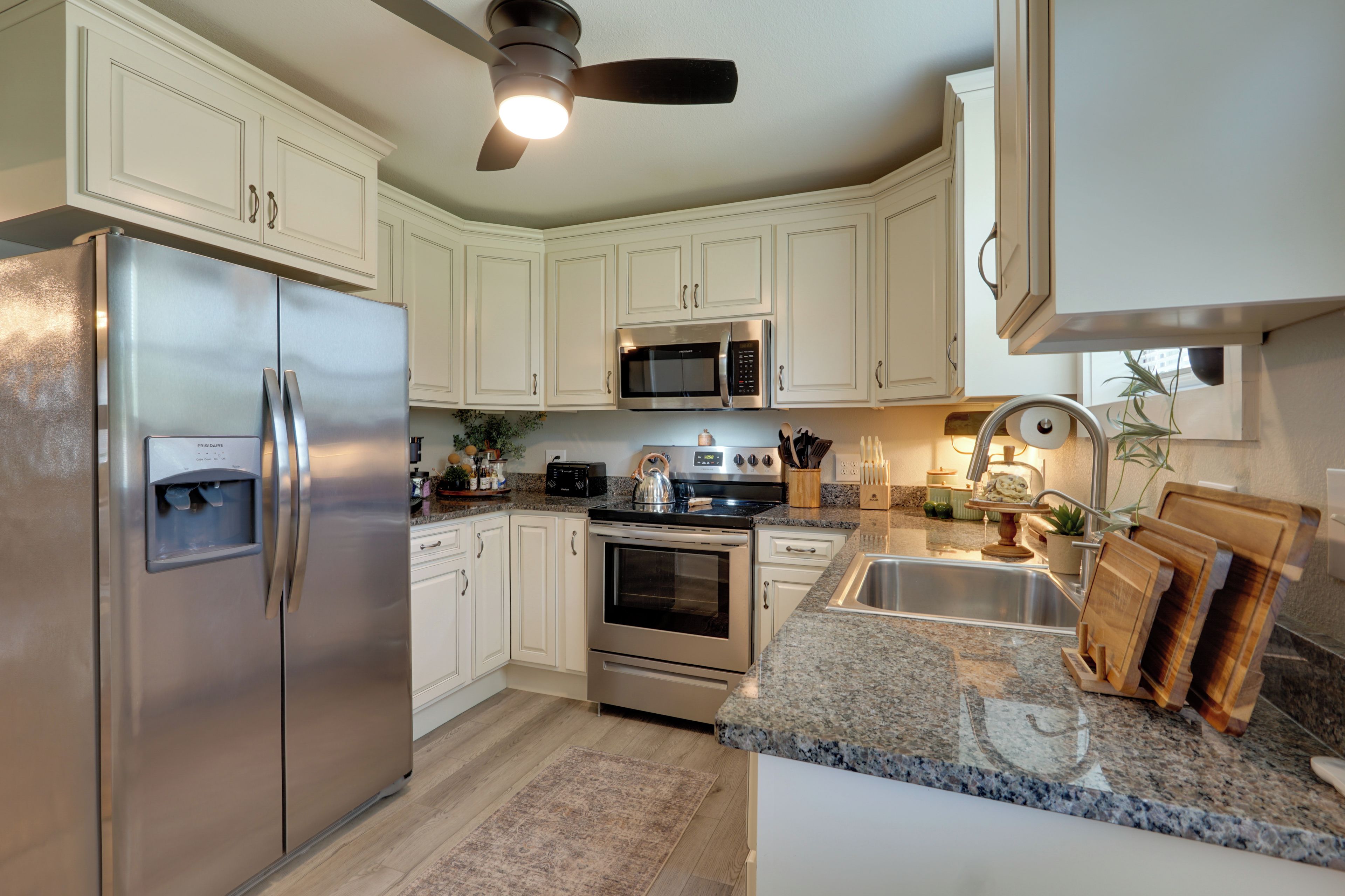 A kitchen with white cabinetry, stainless steel appliances, a granite countertop, and a ceiling fan.