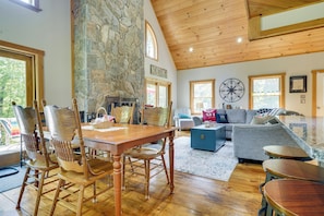 A spacious living area with a stone fireplace, wooden furniture, and a high ceiling with exposed beams.