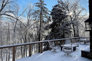 A snow-covered deck with outdoor furniture, surrounded by trees.