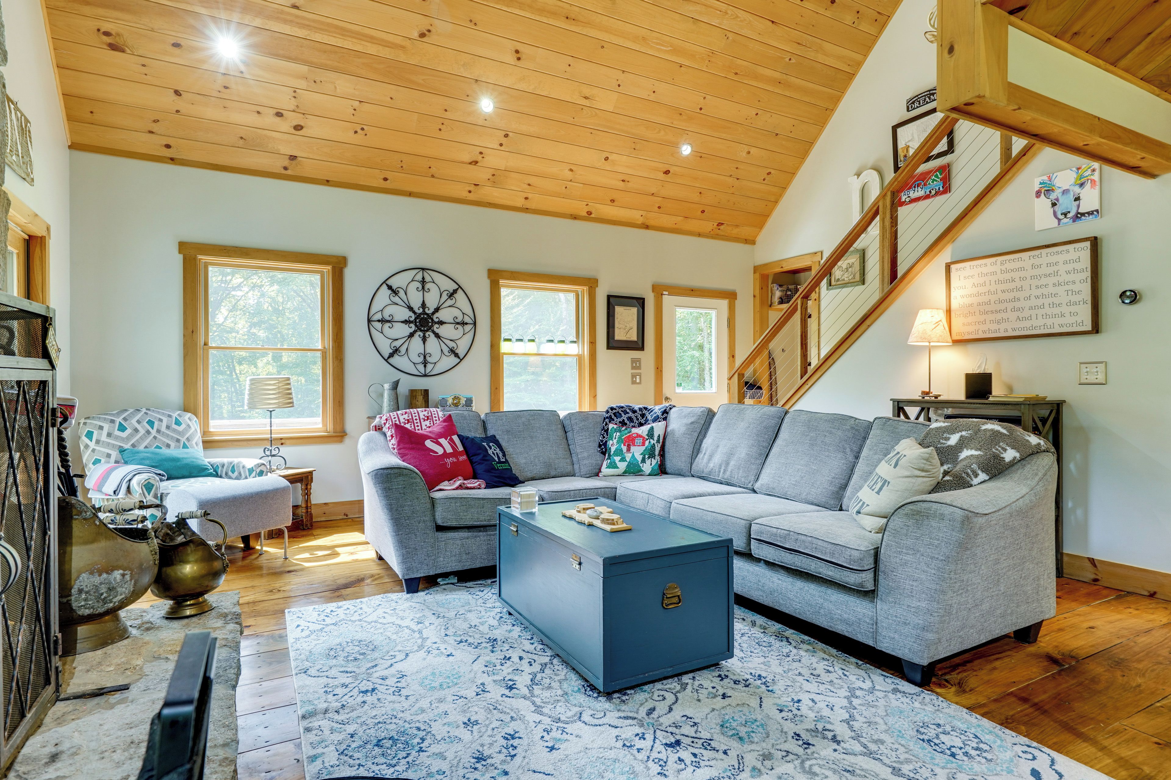 A cozy living room with a wooden ceiling, a grey sofa, a coffee table, and a staircase.