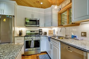 A modern kitchen with white cabinets, stainless steel appliances, and a wooden ceiling.