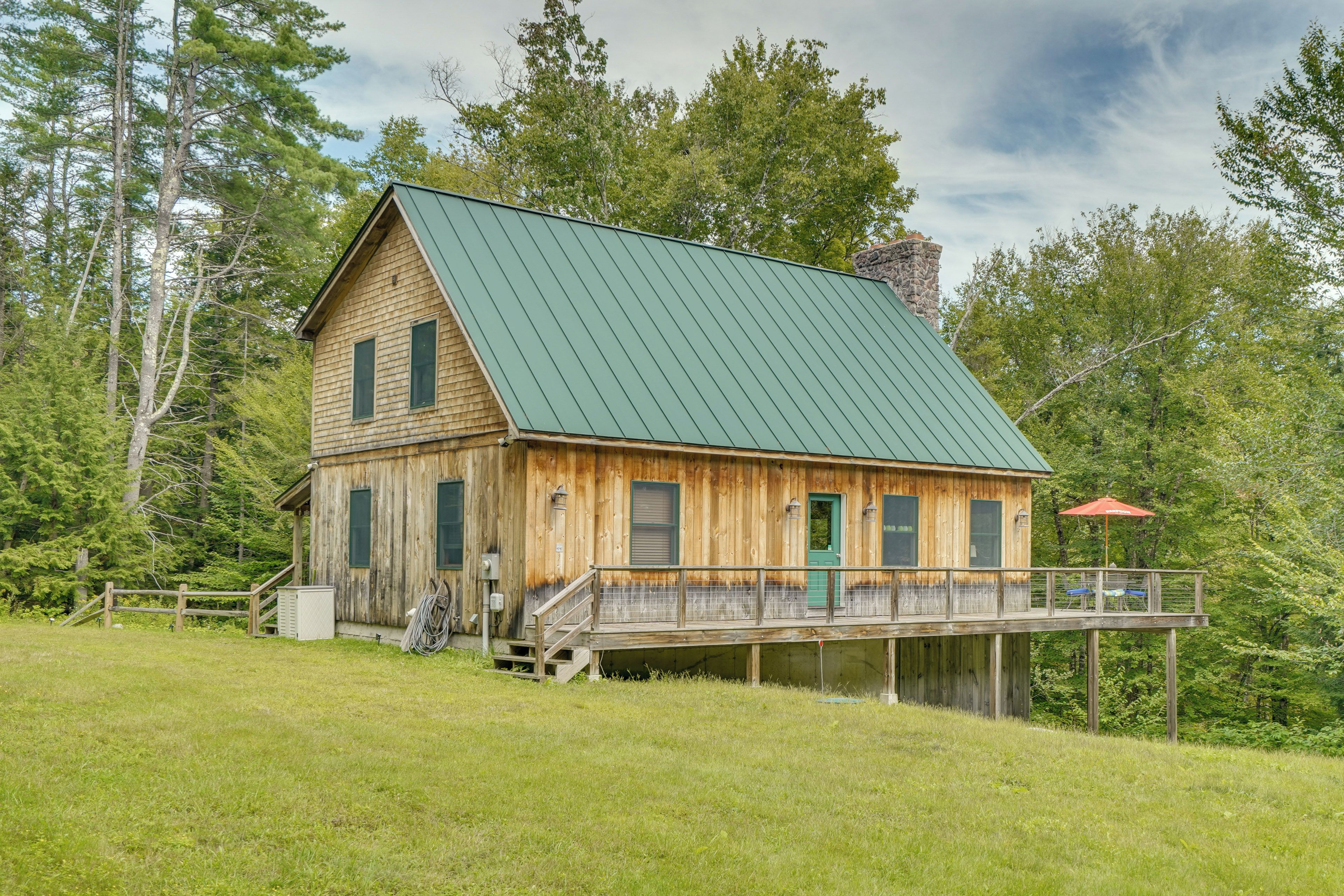 Une cabane en bois avec un toit vert, une terrasse couverte et une cheminée en pierre.