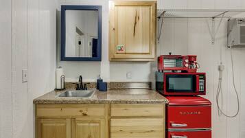 A kitchen with wooden cabinets, a granite countertop, a sink, a double microwave, and a red refrigerator.