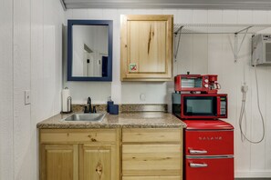 A kitchen with wooden cabinets, a granite countertop, a sink, a double microwave, and a red refrigerator. - Boutique Retreat Minutes From Round Top! (Fayetteville)