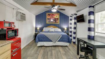 Un dormitorio pequeño con cama, escritorio, microondas rojo y ventilador de techo.
