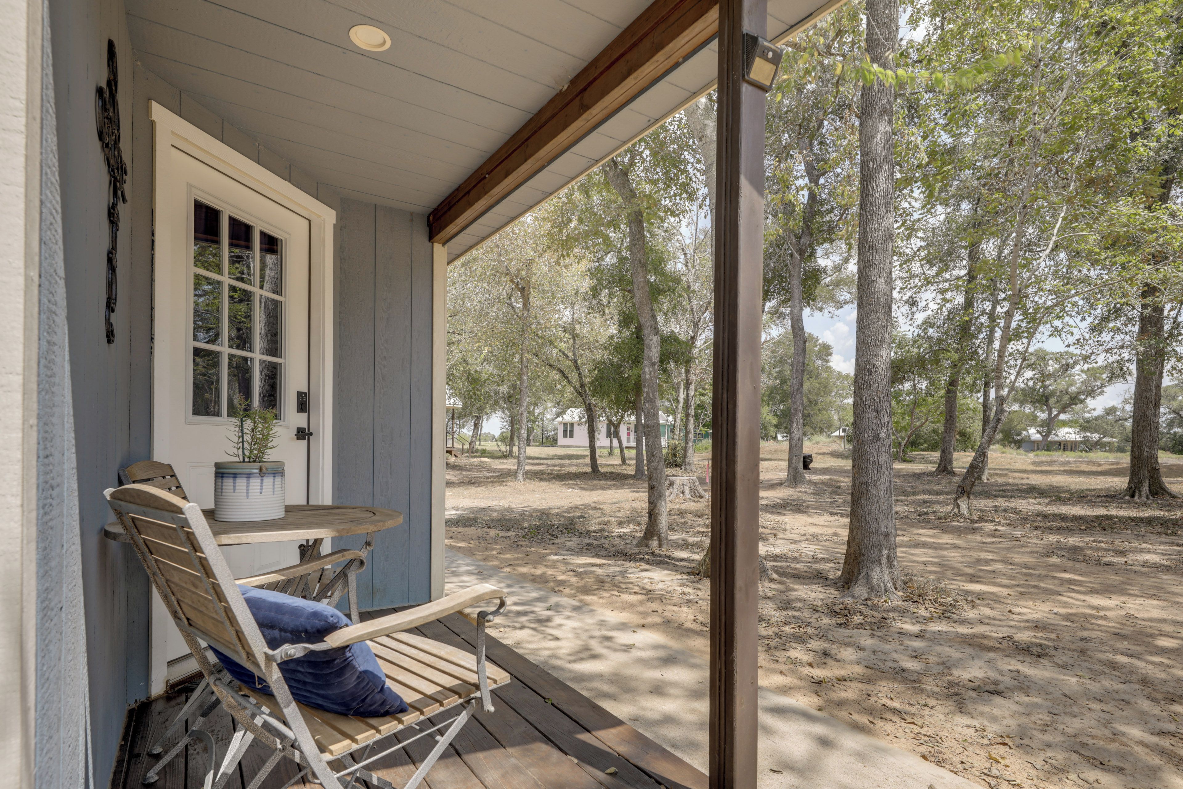 A covered porch with a wooden bench and a table, overlooking a wooded area.