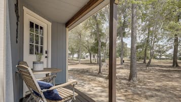 A covered porch with a wooden bench and a table, overlooking a wooded area.