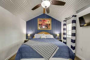A bedroom with a single bed, a ceiling fan, a painting, and a window with curtains.