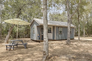A small cabin with a porch, a picnic table, and a covered area with a patterned umbrella.