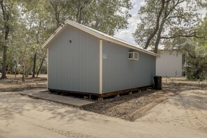 A small, single-story building with a gabled roof, a door, and a window, surrounded by trees and a dirt ground. - Boutique Retreat Minutes From Round Top! (Fayetteville)