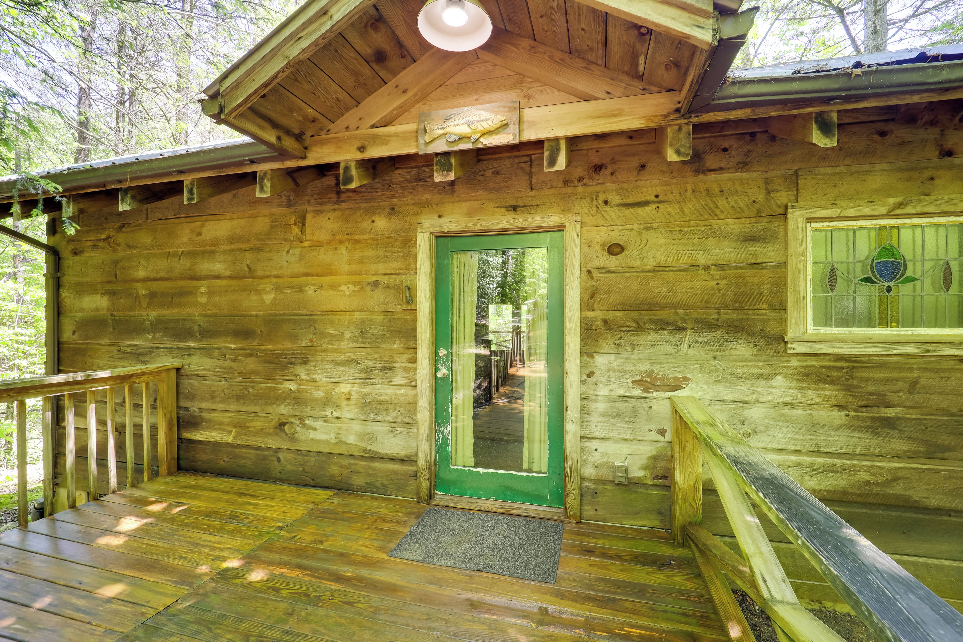 Una cabaña de madera con puerta verde, un muelle de madera y un pequeño porche.