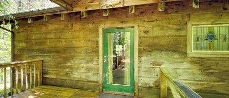 Una cabaña de madera con puerta verde, un muelle de madera y un pequeño porche.