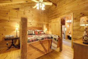 Un dormitorio de cabaña de madera con una cama, dos lámparas de noche, una mesa con lámpara y un jarrón decorativo.