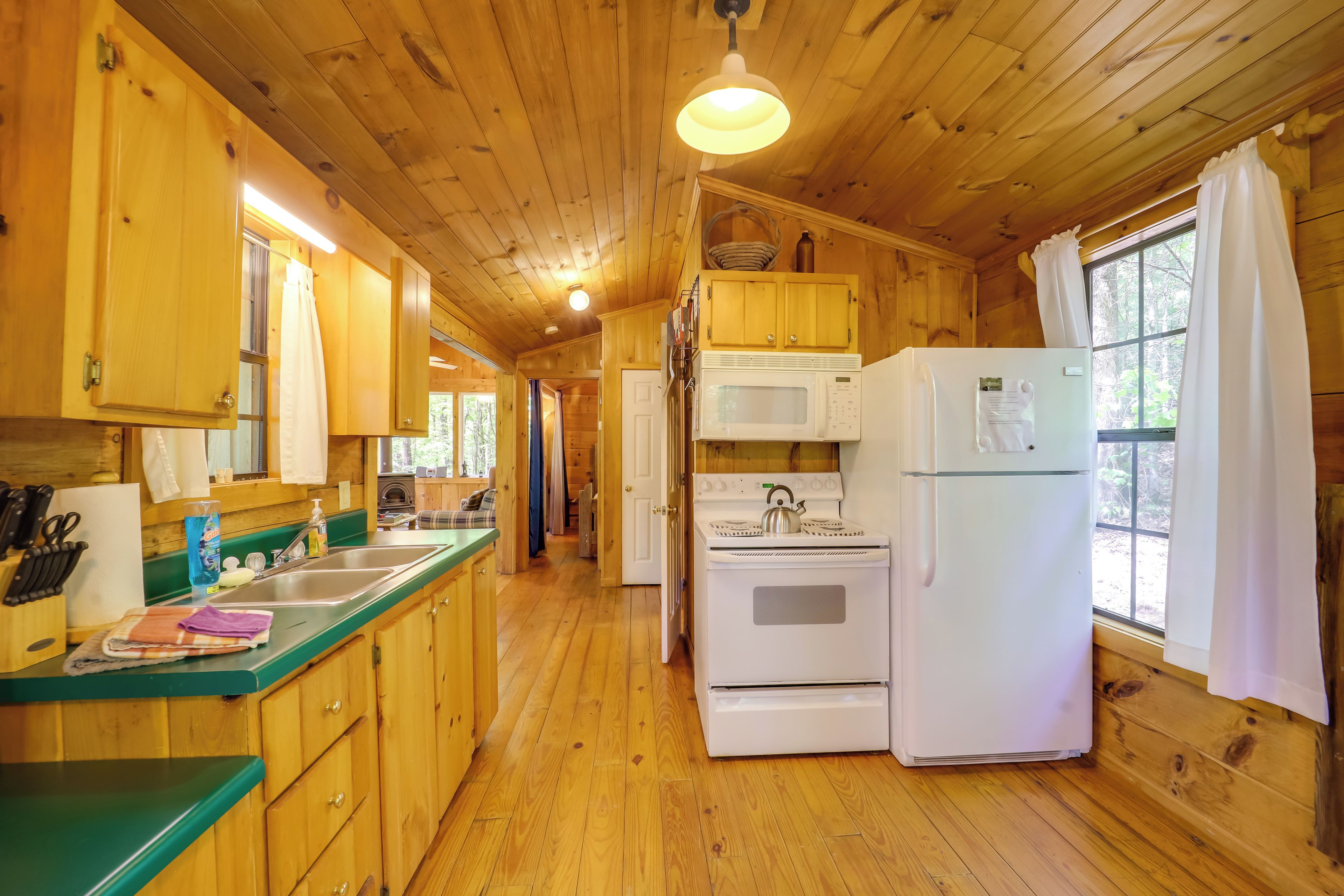 A wooden cabin kitchen with wooden cabinets, a green countertop, a microwave, a stove, and a refrigerator.