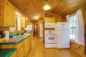 A wooden cabin kitchen with wooden cabinets, a green countertop, a microwave, a stove, and a refrigerator. - Group of 6 Cabins on 92-acre Farm in Marion (Marion)