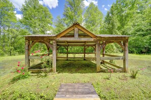 A wooden gazebo with a triangular roof and open sides, surrounded by lush greenery and a pond. - Group of 6 Cabins on 92-acre Farm in Marion (Marion)