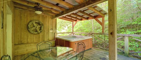 Terraza de madera con mesa y sillas de vidrio, jacuzzi y pared de madera decorada con una cuerda.