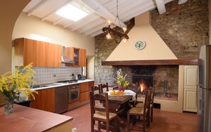 Eine Küche mit Holzschränken, einer Steinsäule, einem Kamin und einem Essbereich mit Stühlen und einem Tisch.