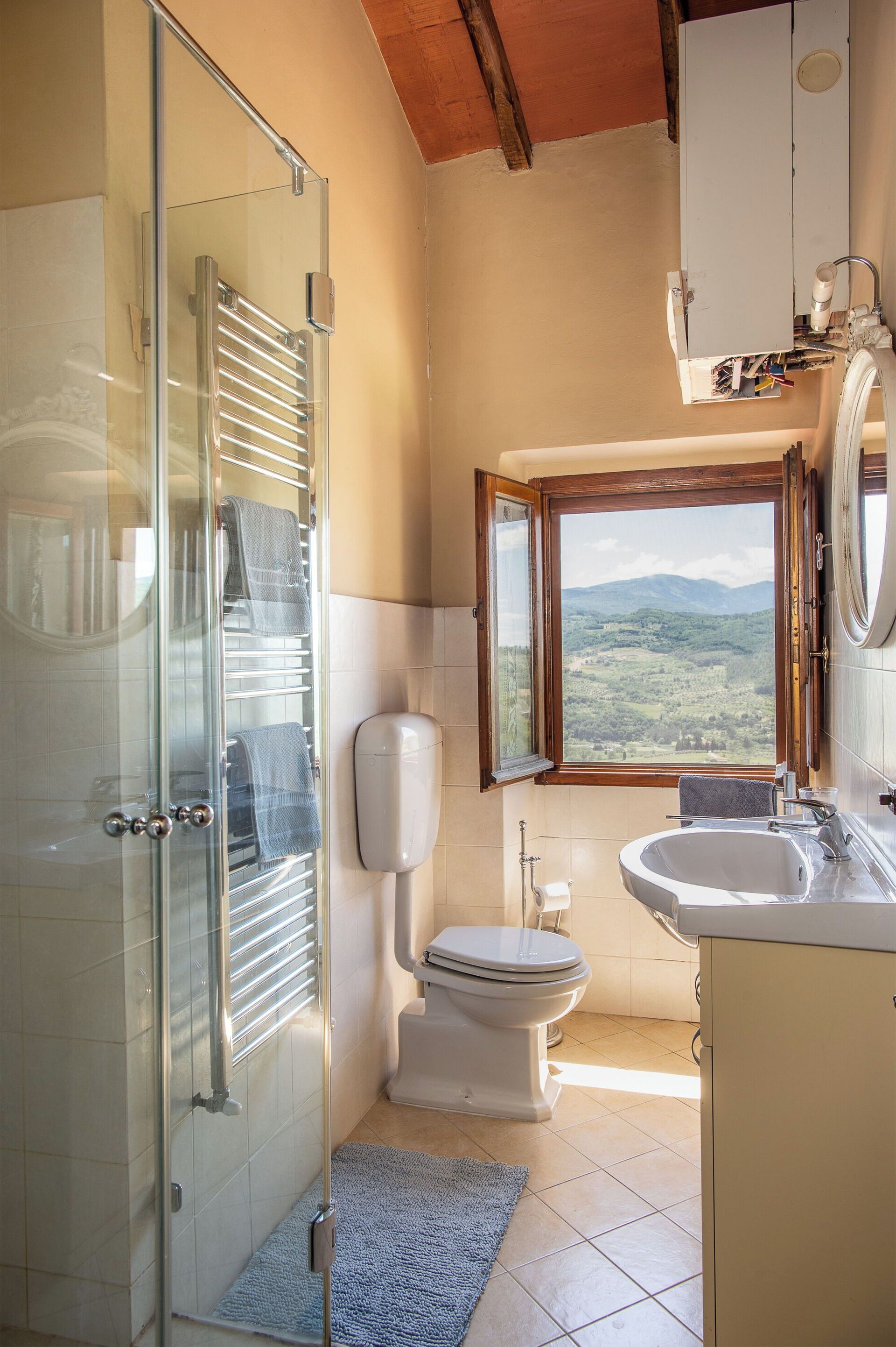 Ein Badezimmer mit Duschkabine aus Glas, Toilette, Waschbecken und einem Fenster mit Blick auf die Berge.