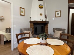 Ein gemütliches Wohnzimmer mit Kamin, zwei Sofas, einem Esstisch mit Platzsets und gerahmten Bildern an den Wänden.