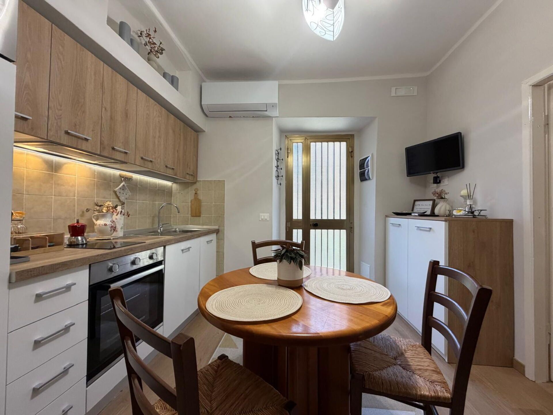 A compact kitchen with a dining area, wooden cabinets, a built-in oven, and a television on the wall.