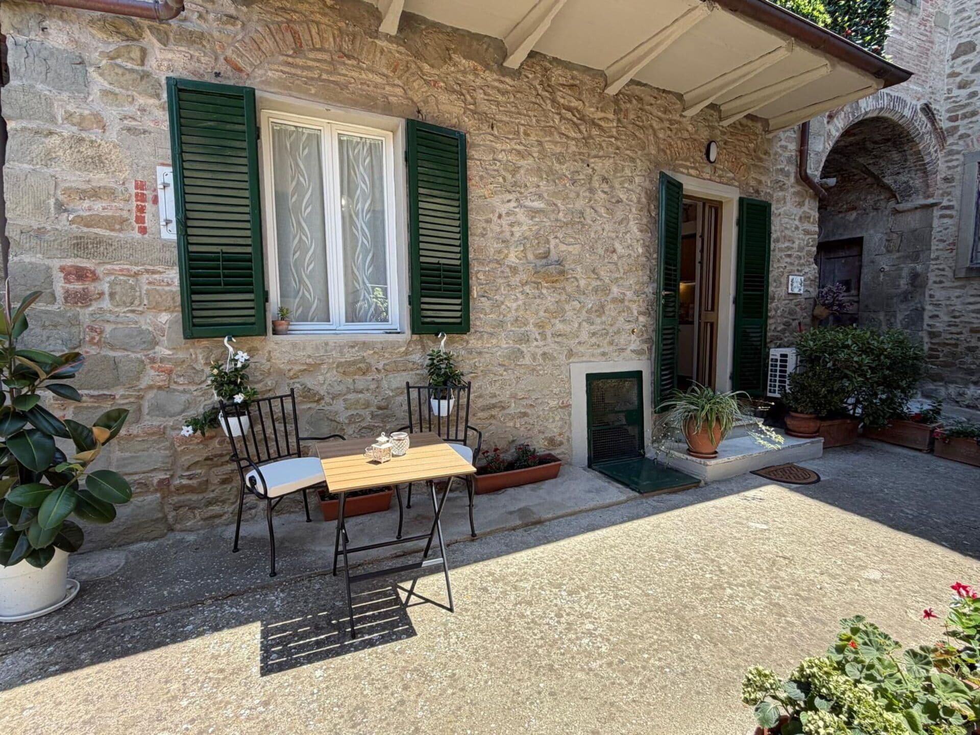 A stone building with a wooden table and chairs outside, a door, and potted plants.