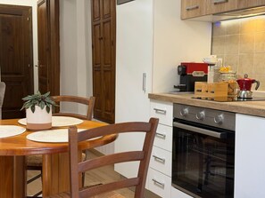 Eine Küche mit Esstisch, Stühlen, einer Kaffeemaschine, einem Wasserkocher und einem Backofen.