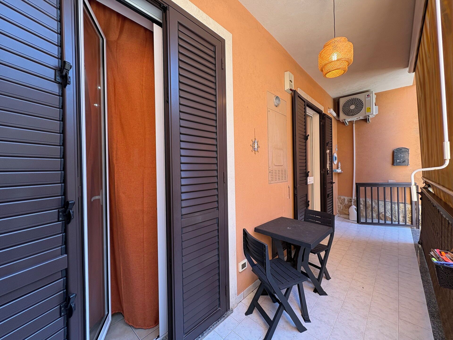 Un balcon avec une table et des chaises, un luminaire suspendu et un appareil de climatisation fixé au mur.