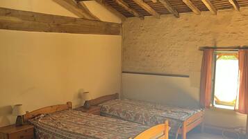 A room with wooden beams, a bed with floral bedding, a nightstand, and a window with curtains.