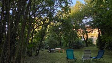 Un espace extérieur aménagé avec une table et des chaises, entouré d’arbres et d’herbe.