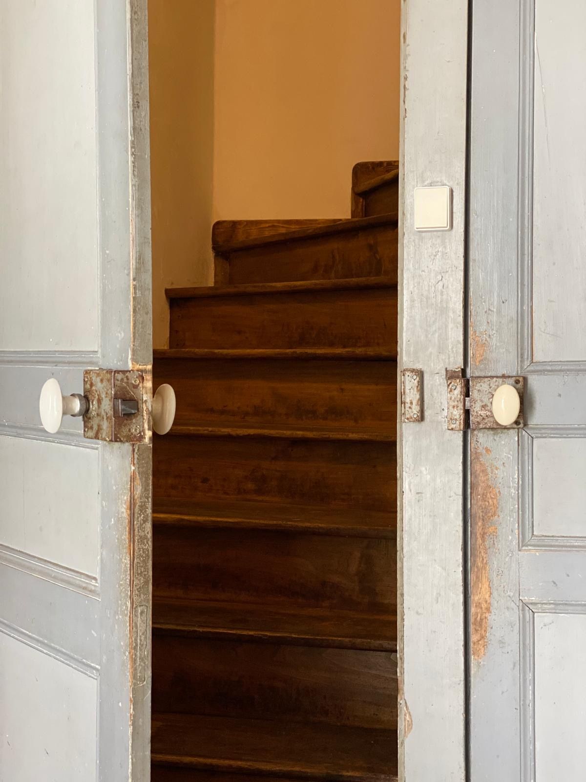 A wooden staircase with a metal handrail and a door with a white handle.