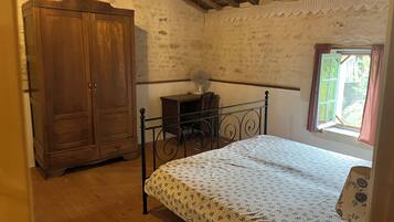 A bedroom with a wooden wardrobe, a metal bed frame, a bedside table with a lamp, and a window with curtains.